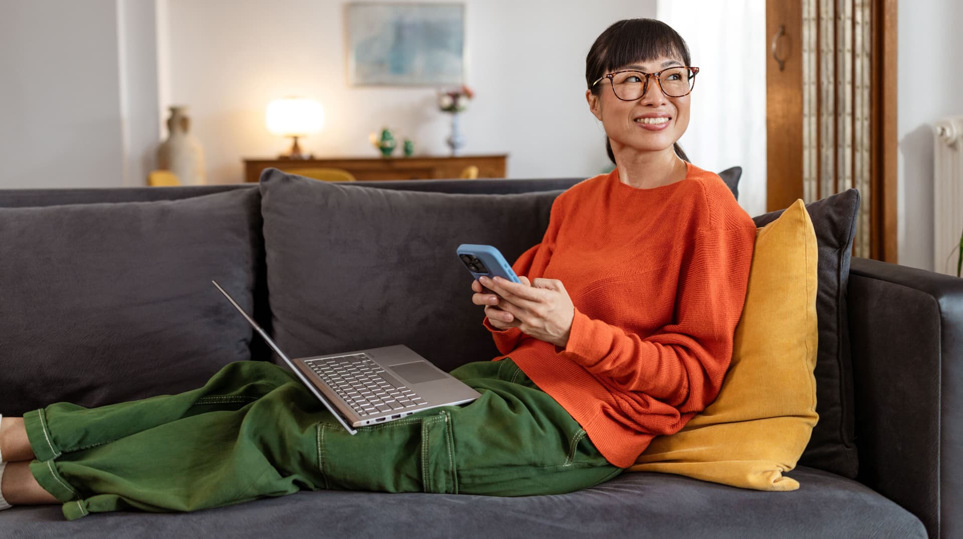 Lächelnde Frau auf Sofa mit Laptop auf dem Schoß