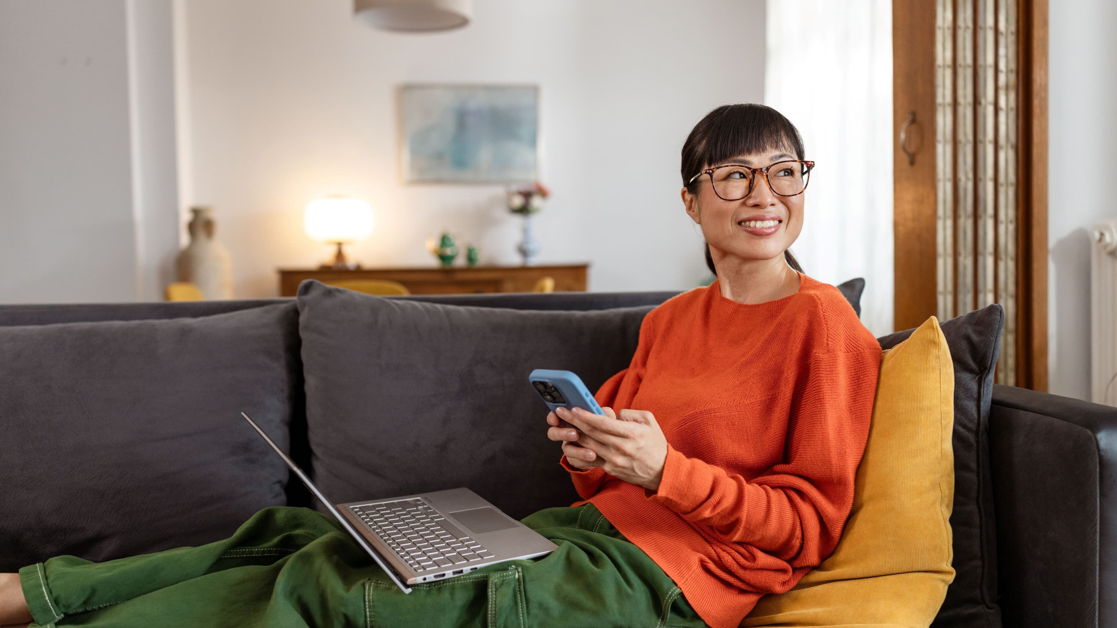 Lächelnde Frau auf Sofa mit Laptop auf dem Schoß