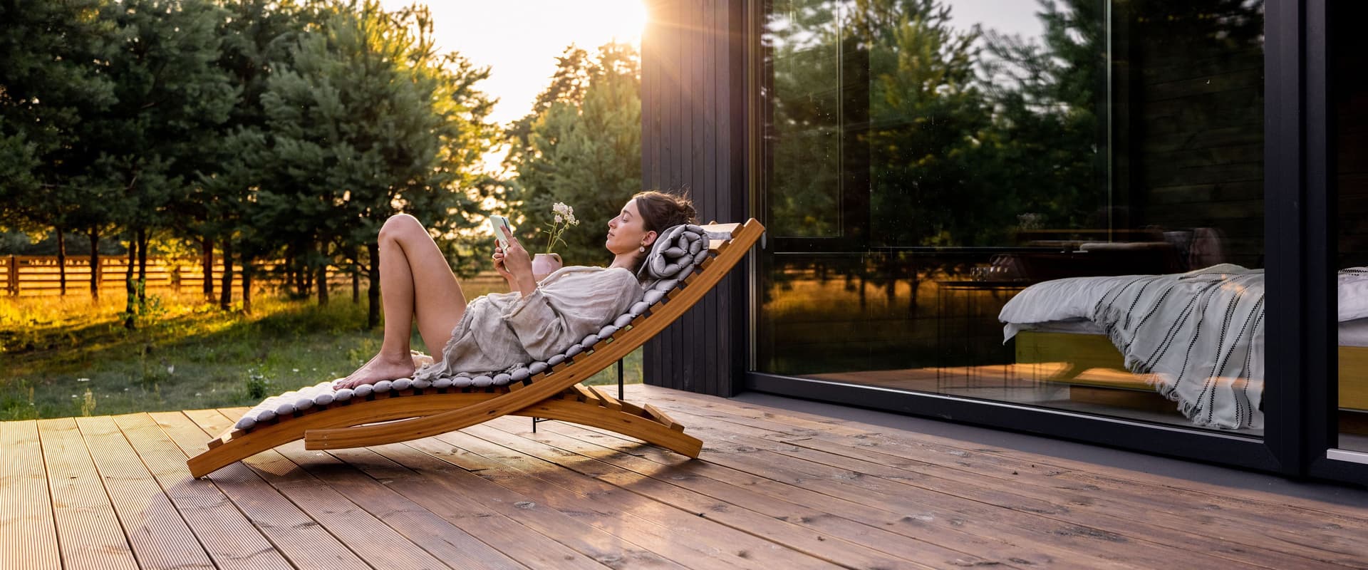 Frau liegt auf einer Sonnenliege auf der Holzterrasse eines Hauses. 