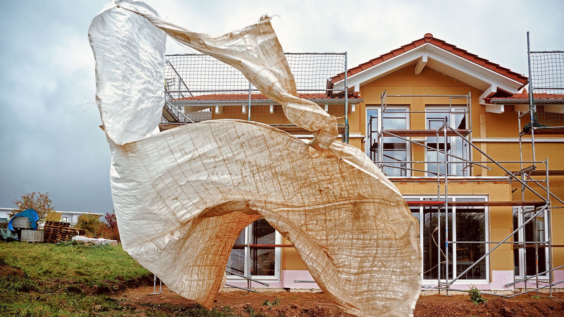 Baugerüstplane flattert losgelöst vom Rohbau im Wind.