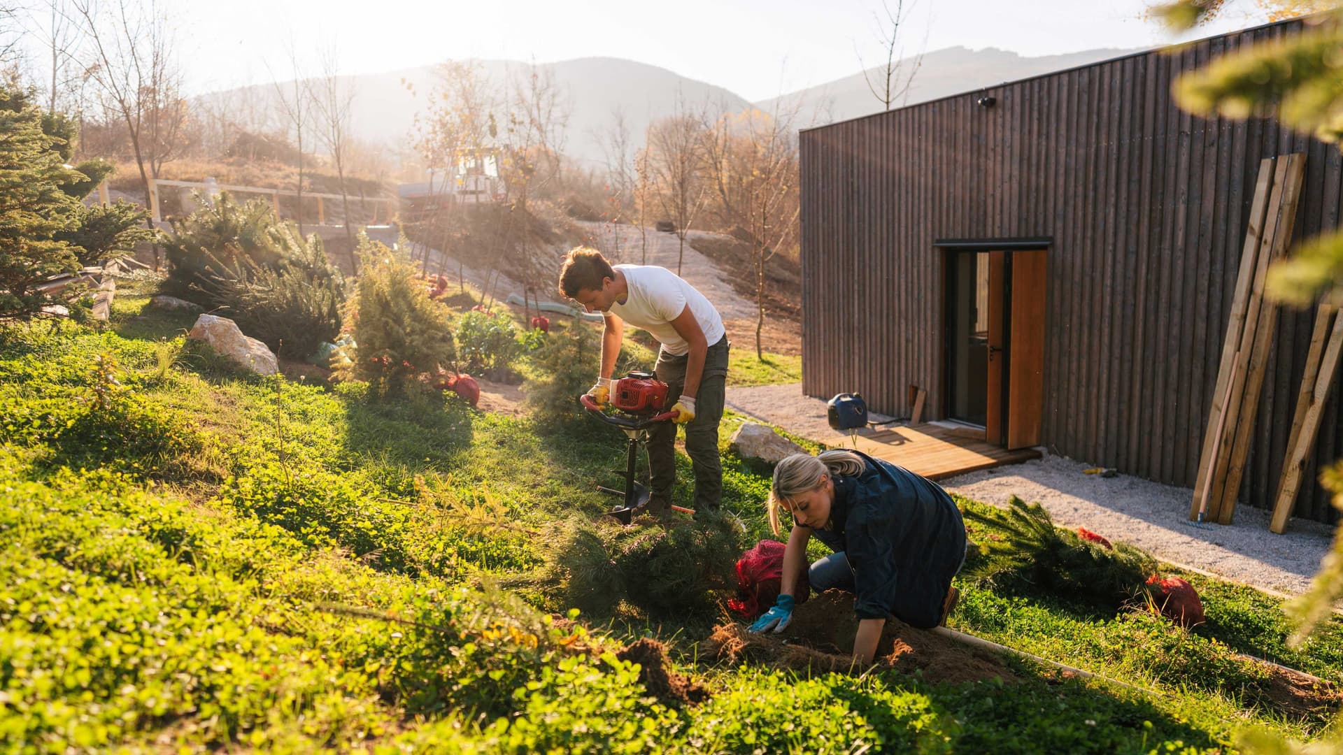 Eine junge Frau und ein junger Mann legen an ihrem Holzhaus einen Garten an.