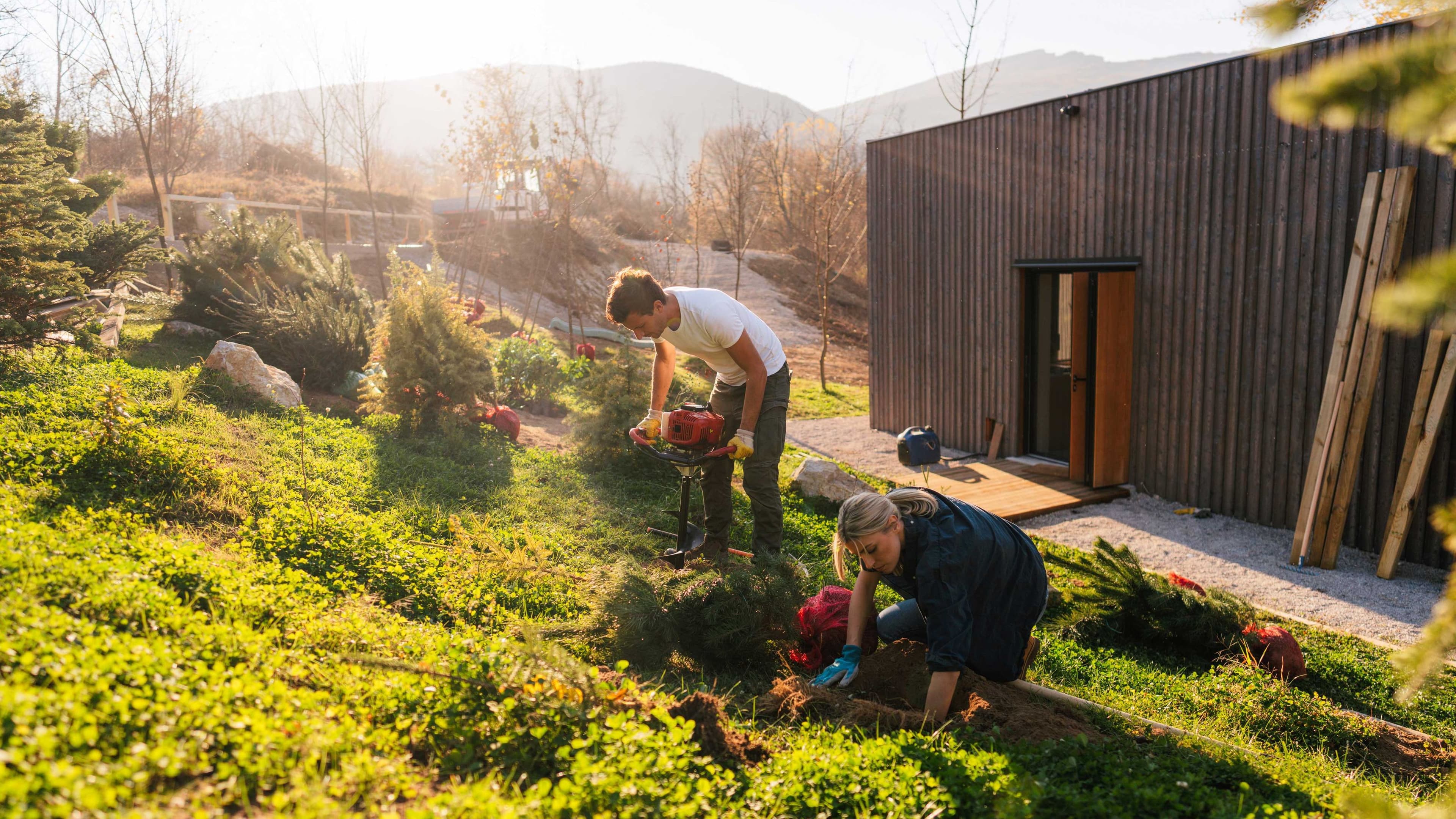 Eine junge Frau und ein junger Mann legen an ihrem Holzhaus einen Garten an.