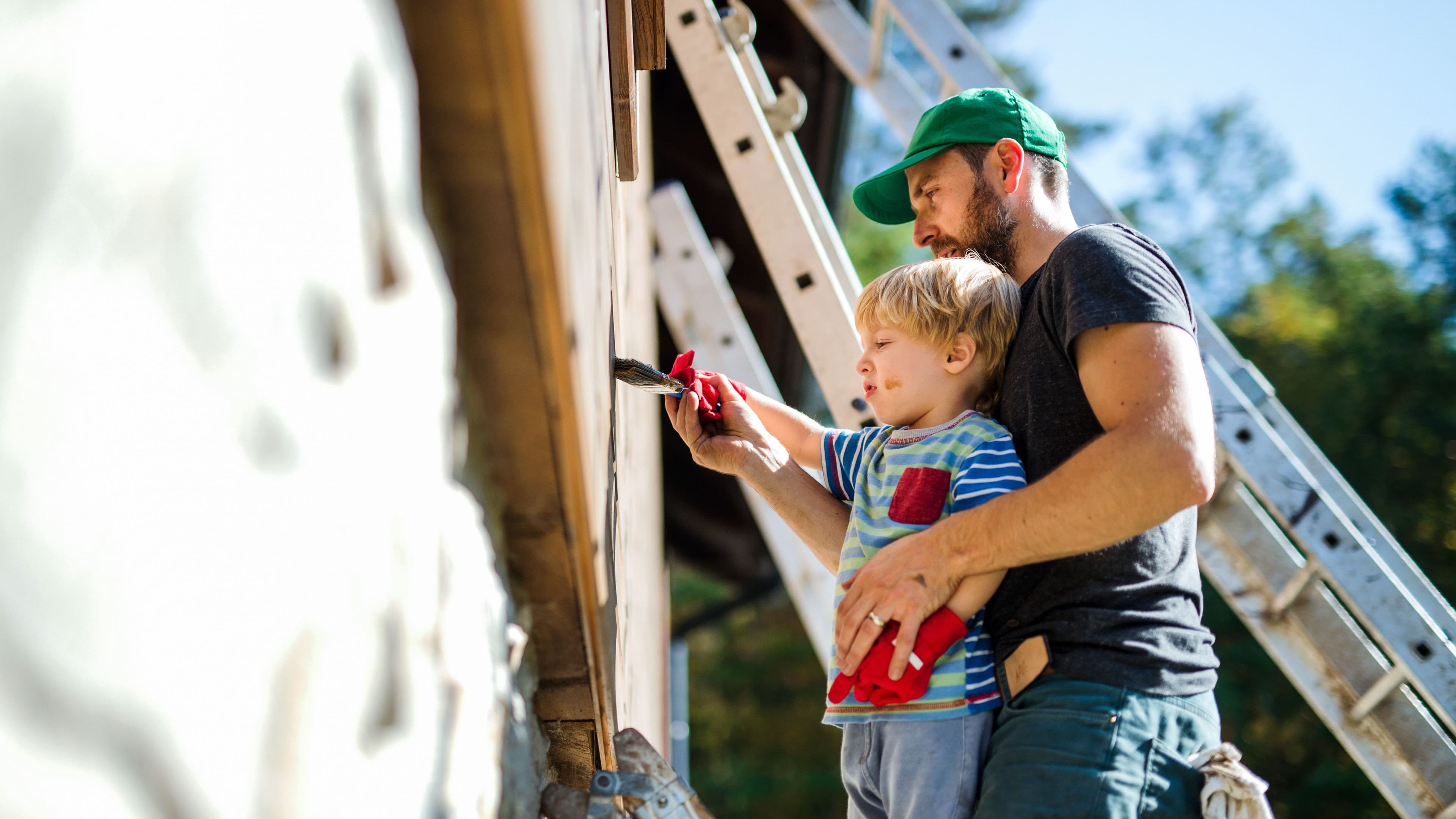 Vater- und Kleinkind streichen einen Holzhaus