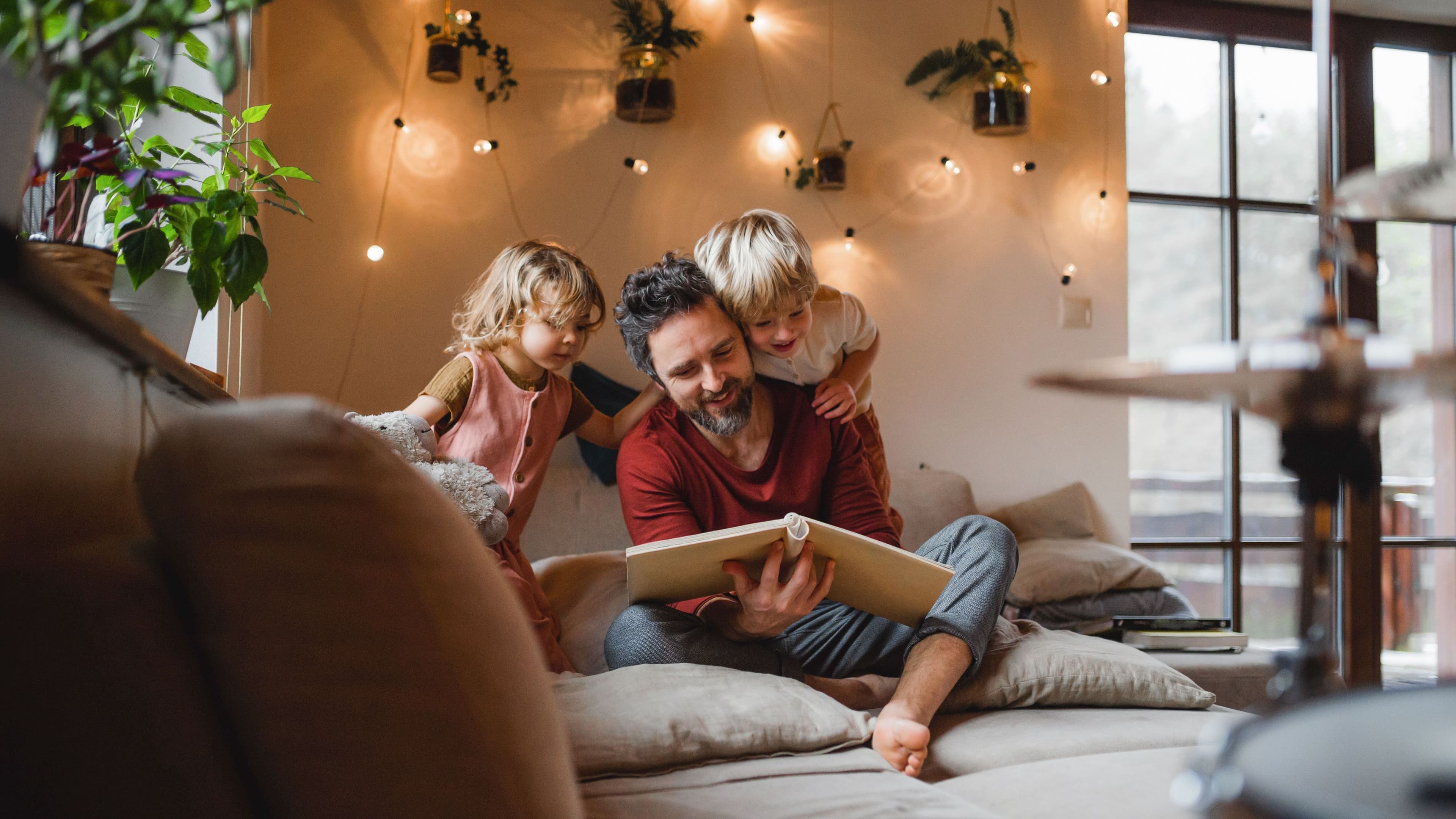 Ein Mann und zwei Kinder sitzen auf einem Sofa und schauen in ein Buch.