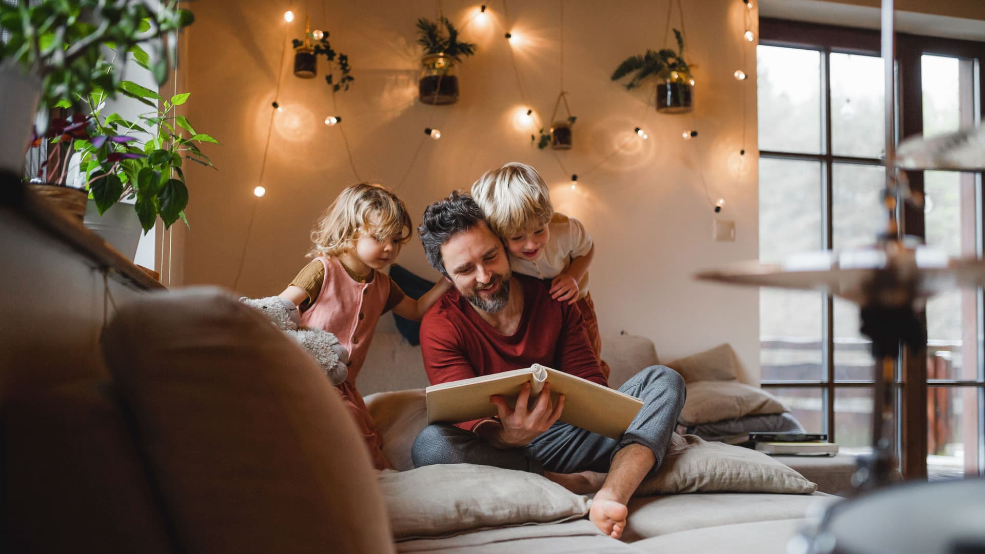 Ein Mann und zwei Kinder sitzen auf einem Sofa und schauen in ein Buch.