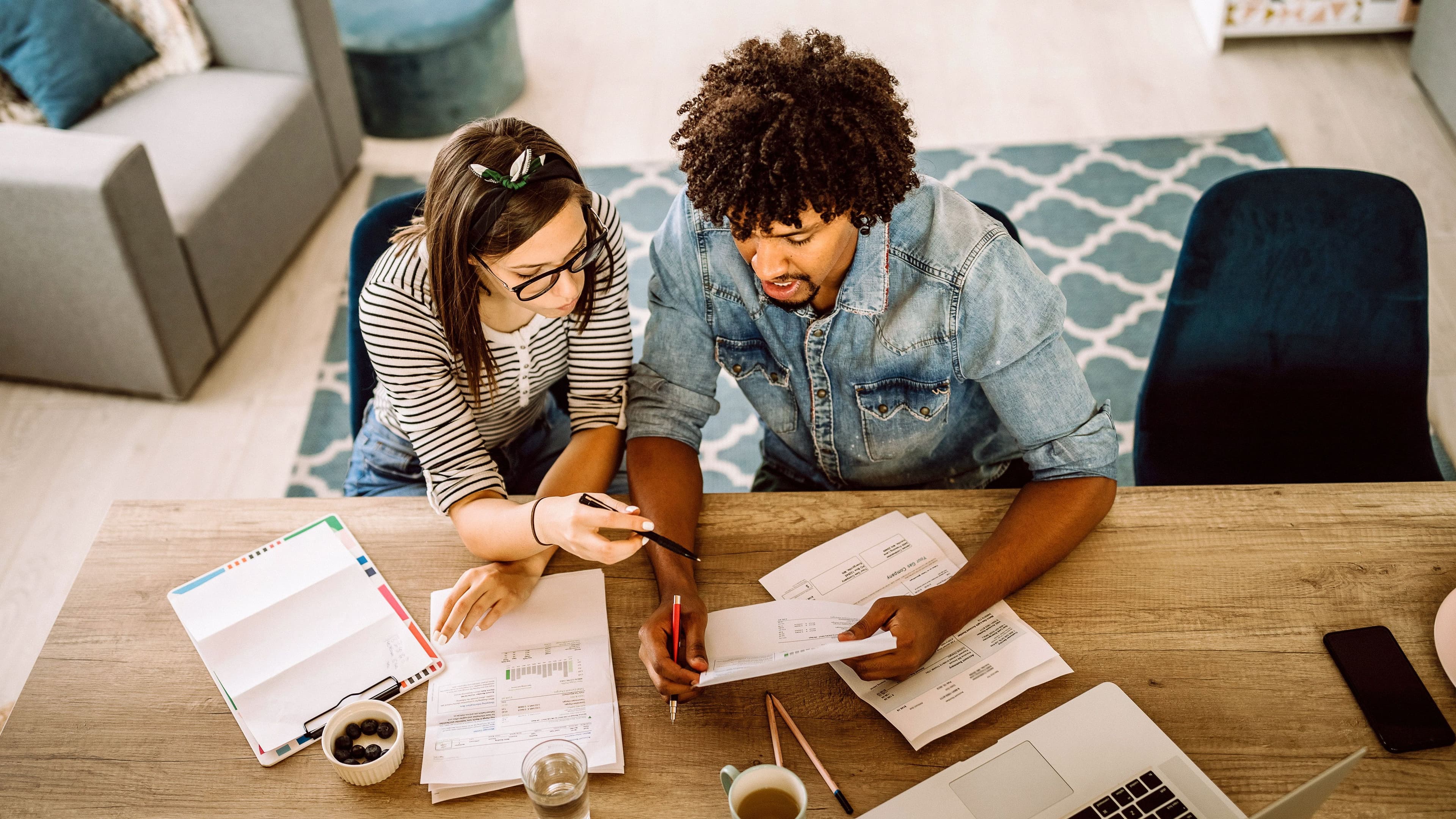Blick von oben auf ein junges Paar, das an einem Tisch gemeinsam Unterlagen bespricht.