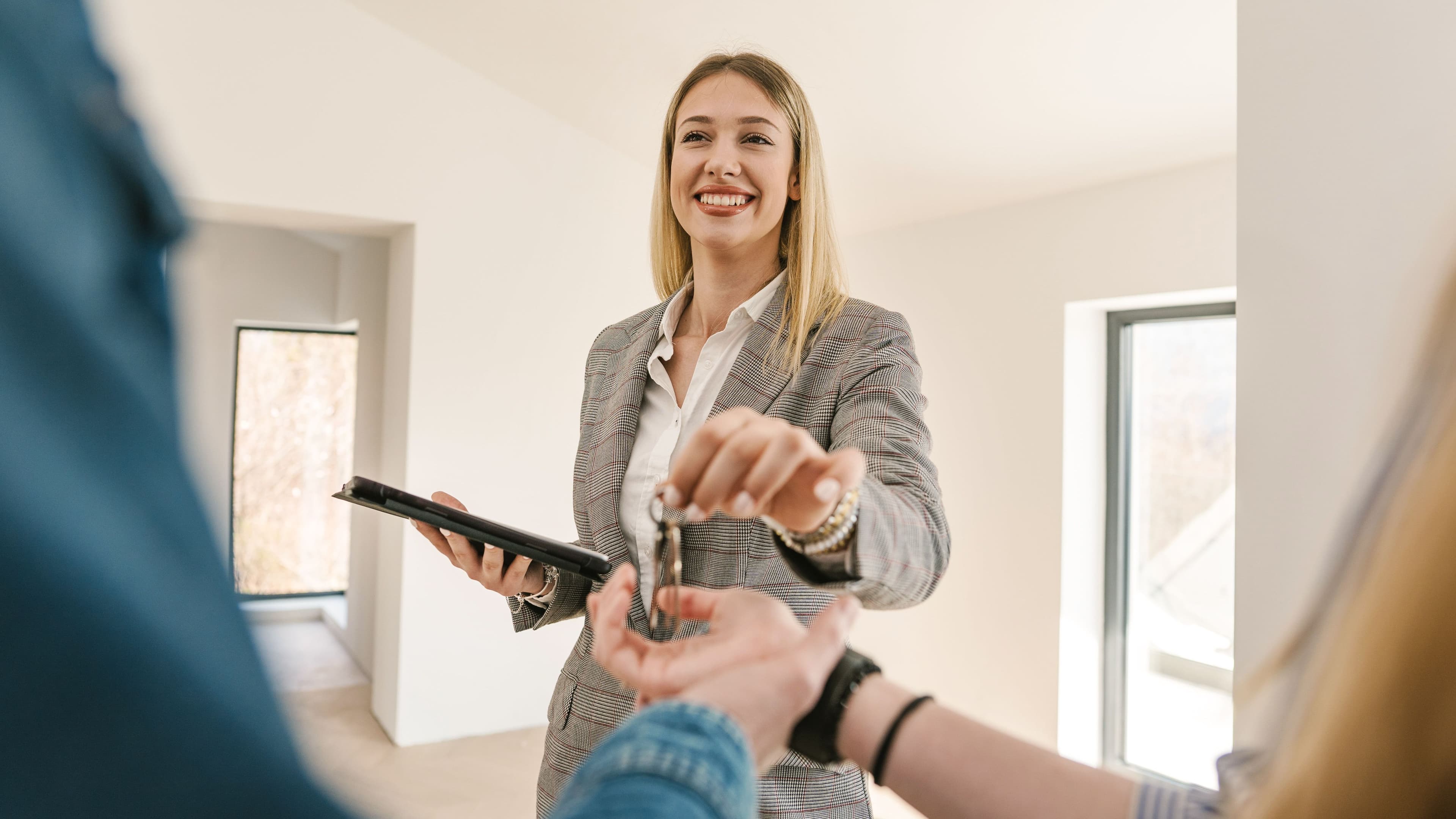 Eine lächelnde Immobilienmaklerin während der Schlüsselübergabe. Im Vordergrund sind zwei Hände zu sehen.