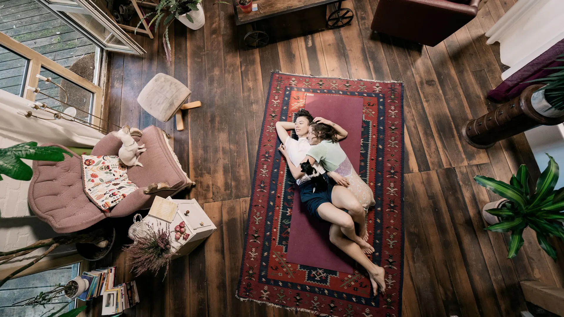 Blick von oben auf ein junges Paar, das auf dem Wohnzimmer auf einem Teppich am Boden liegt.