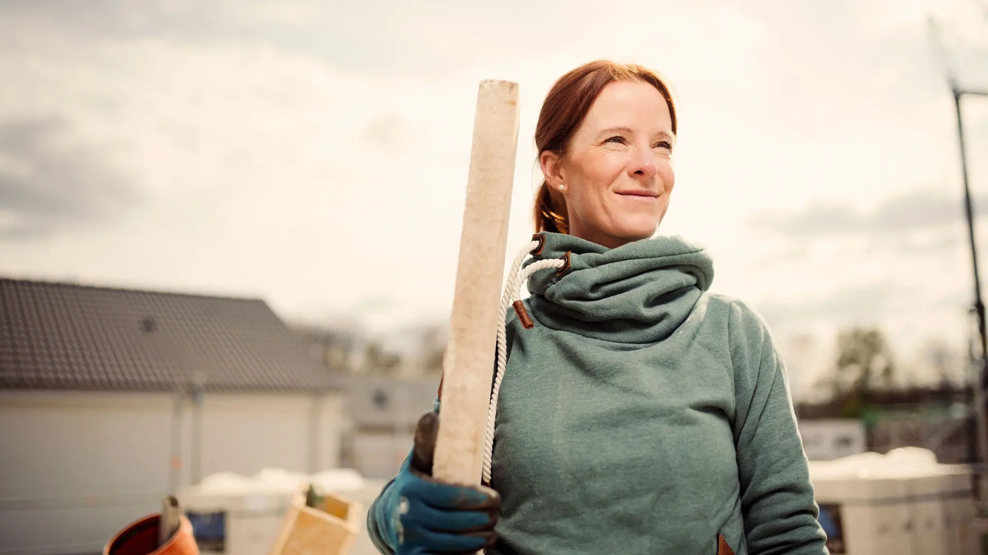 Eine Frau steht mit einem Stück Holz in der Hand auf einer Baustelle.
