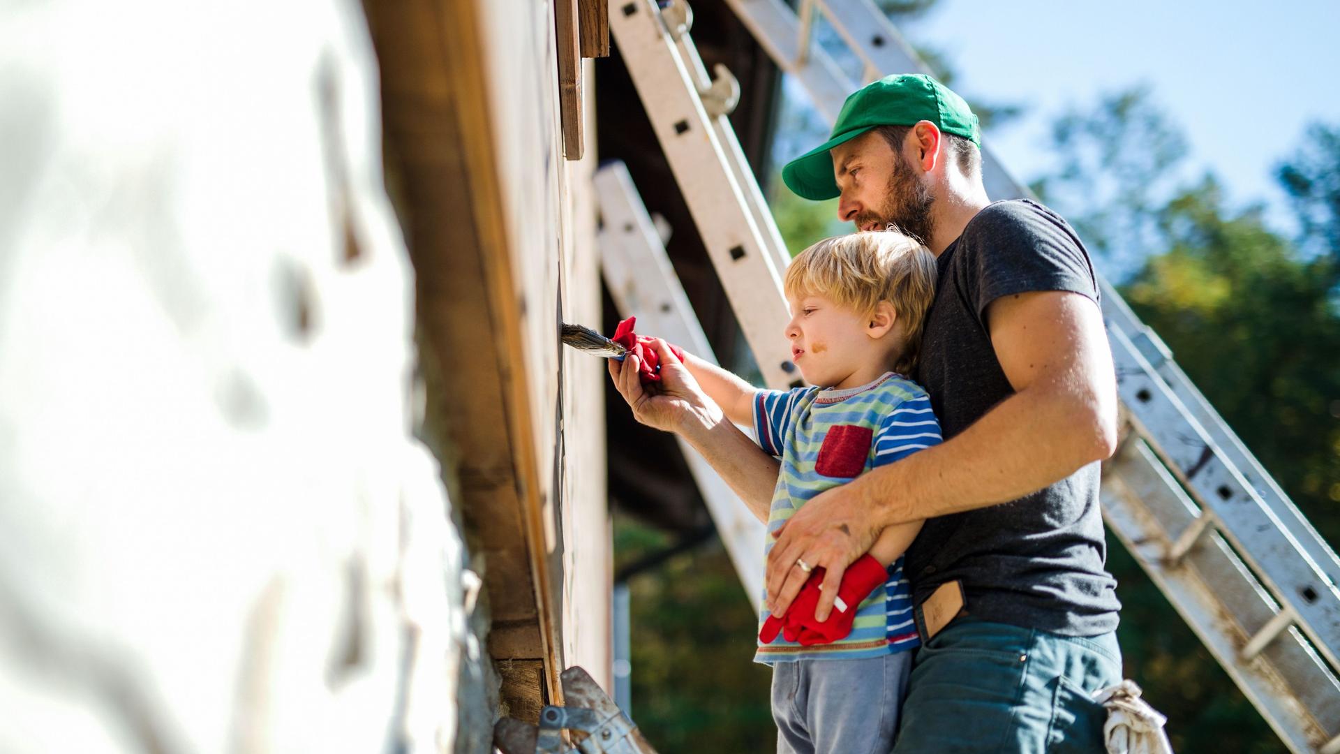 Vater- und Kleinkind streichen einen Holzhaus